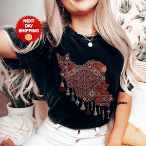 May include: Black t-shirt featuring a detailed map of Iran, filled with a colorful rug design. The shirt has decorative tassels and the word "BLACK" at the bottom. A red circle with "NEXT DAY SHIPPING" is visible.