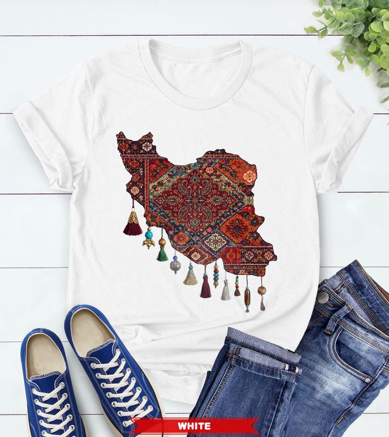 May include: White t-shirt featuring a detailed graphic of the Iran map filled with a traditional rug design in red, blue, and gold. The design includes decorative tassels. Blue sneakers and jeans are also visible.
