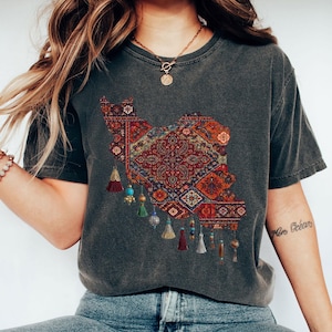 May include: Dark gray heather t-shirt featuring a detailed, colorful rug design in the shape of a country. The design includes intricate patterns in red, orange, and blue, with decorative tassels hanging below. The text "DARK GRAY HEATHER" is at the bottom.