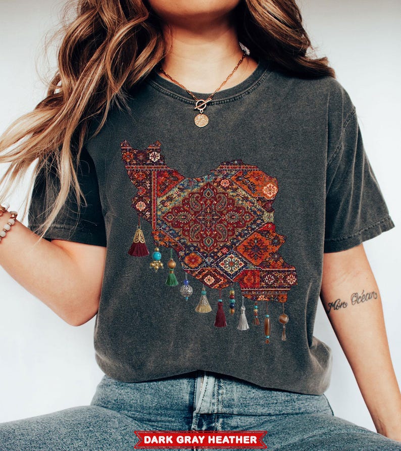 May include: Dark gray heather t-shirt featuring a detailed, colorful rug design in the shape of a country. The design includes intricate patterns in red, orange, and blue, with decorative tassels hanging below. The text "DARK GRAY HEATHER" is at the bottom.