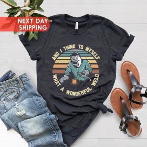 May include: Black t-shirt with a retro-style graphic of a welder with the text "And I think to myself what a wonderful weld".