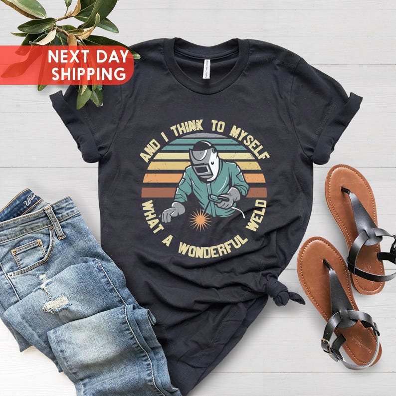 May include: Black t-shirt with a retro-style graphic of a welder with the text "And I think to myself what a wonderful weld".
