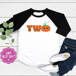 May include: White and black baseball tee shirt with a pumpkin with a spiderweb design and the word "TWO" on the front.