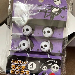 May include: A package of four Nightmare Before Christmas themed food picks. The picks are white with a black Jack Skellington face on the top. The package is purple and black with the text "The Nightmare Before Christmas" and "Halloween Lunch Picks" in Japanese.