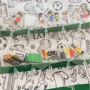 以下が含まれることがあります： 緑と白のデザインのサッカーをテーマにしたクラフトキット。キットには、ミニチュアのサッカー選手、サッカーボール、サッカースパイクが含まれています。「Soccer」の文字が緑色のバナーに白で印刷されています。