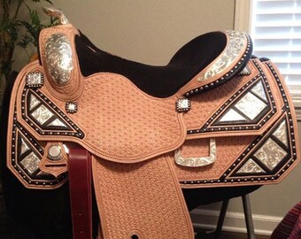 May include: A brown leather saddle with silver and black accents. The saddle has a black seat and a silver concho on the front.