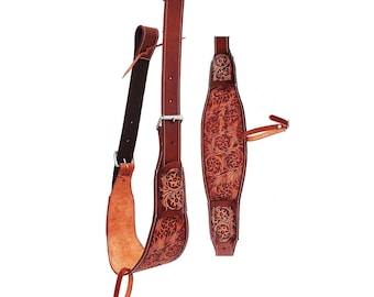 May include: A set of brown leather horse tack, including a stirrup strap and a breast collar. The leather is tooled with a floral pattern. The stirrup strap has a black underside and a silver buckle. The breast collar has a silver buckle and a leather strap.