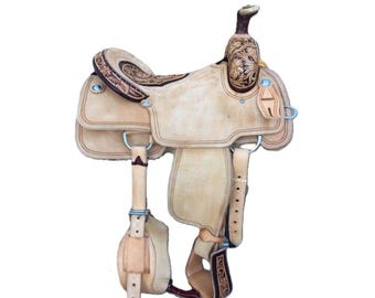 May include: A tan leather saddle with intricate floral tooling. The saddle features a  brown leather seat and a high cantle. The saddle is in good condition and would be a great addition to any horse owner's tack room.