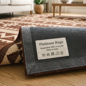 May include: A rolled-up brown and cream-colored area rug with a geometric pattern. The rug's underside is gray, with a label that reads "Platinum Rugs, Handtufted 100% wool pile, Made in India."