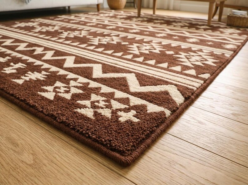 May include: Brown and cream-colored area rug with a geometric pattern. The rug features repeating shapes and lines in a tribal design. The rug is rectangular and has a dark brown border.