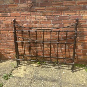 May include: A dark brown metal headboard featuring a curved top rail and a lower horizontal bar. The frame consists of vertical spindles with decorative finials at the top and rounded accents at the base, creating a structured, open-work design.