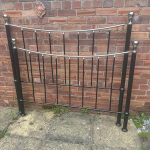 May include: A black metal headboard featuring two horizontal curved silver bars and vertical black spindles. The structure includes four tall vertical posts topped with rounded silver finials, creating a symmetrical frame for a bed setup.