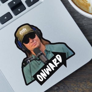 May include: A laptop with a sticker of a person wearing a hat and sunglasses, holding a microphone, with the word "ONWARD" in a white font on a black arrow. A cup of coffee with latte art is next to the laptop.