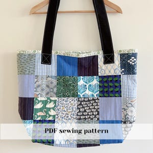 Op de afbeelding: Een patchwork tote bag met een verscheidenheid aan blauwe en witte stoffen vierkanten met patronen. De tas heeft zwarte handvatten en de tekst "PDF sewing pattern" onderaan.