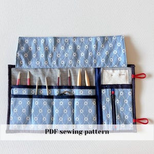 Può includere: Un astuccio per aghi da cucito con motivo floreale blu e bianco con vari strumenti di cucito all'interno. Il rotolo ha più tasche e uno scomparto con cerniera. Il testo "PDF sewing pattern" è in basso.