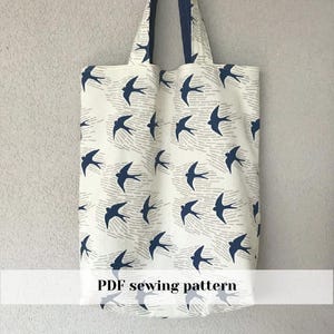 Op de afbeelding: Een witte draagtas met een herhalend patroon van marineblauwe zwaluwen en grijze stippellijnen. De tas heeft marineblauwe handvatten en de tekst "PDF sewing pattern" onderaan.