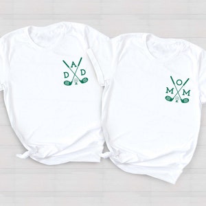 May include: Two white t-shirts with green golf club and ball designs. The left shirt says "DAD" and the right shirt says "MOM".