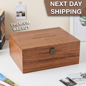 May include: A rectangular walnut keepsake box with a hinged lid and a metal latch. The lid is engraved with the text PRECIOUS MEMORIES, GRACE and ELLIOT, and est. 2014. The wood features a natural grain pattern in medium brown tones.