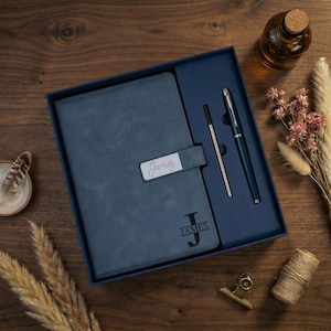 May include: A blue notebook with a magnetic closure strap featuring the name James, and a matching blue pen set inside a blue gift box. The notebook cover is embossed with a large letter J and the name James in a dark, bold font.