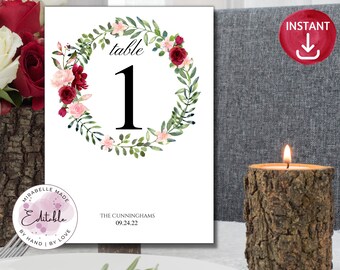 May include: A white printable table number card with a floral wreath design. The wreath is made of green leaves and pink and red flowers. The number "1" is in the center of the wreath. The text "table" is above the number. The text "The Cunninghams 09.24.22" is at the bottom of the card.