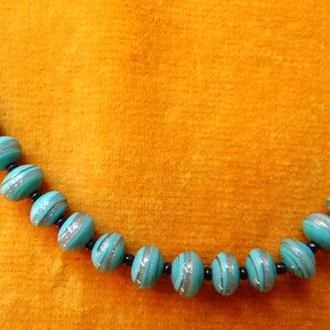 May include: A turquoise blue necklace with silver and black accents. The beads are round and have a striped pattern.