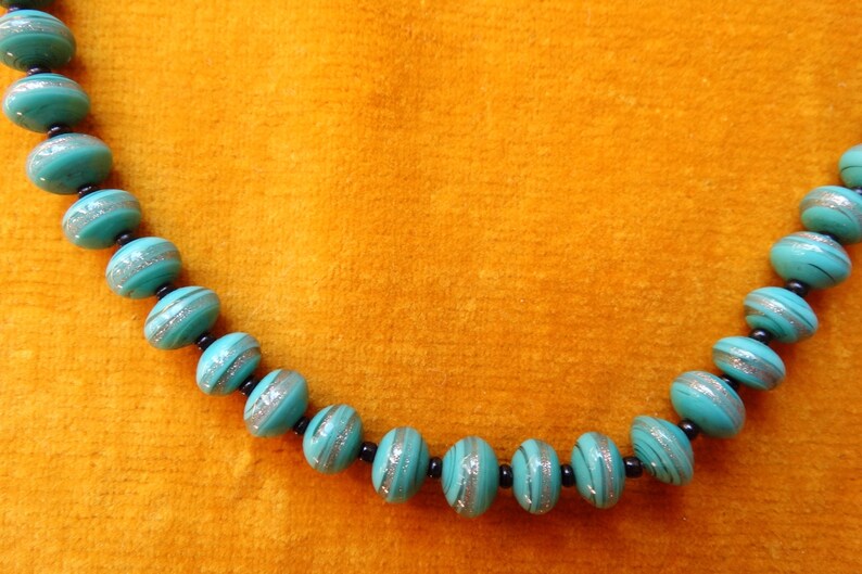 May include: A turquoise blue necklace with silver and black accents. The beads are round and have a striped pattern.