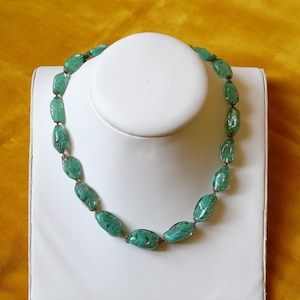 May include: A green glass bead necklace with a marbled pattern. The beads are oval shaped and strung on a silver wire.