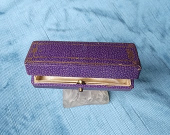May include: A purple velvet jewelry box with a gold trim and a white satin interior. The box is open and the lid is propped up.