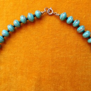 May include: A turquoise and silver beaded necklace with a silver clasp. The beads are round and have a striped pattern.
