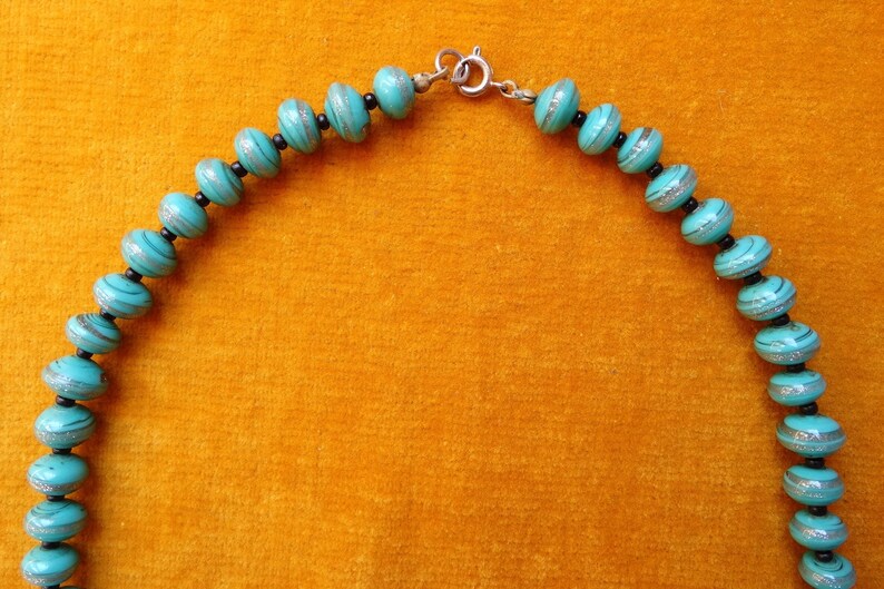 May include: A turquoise and silver beaded necklace with a silver clasp. The beads are round and have a striped pattern.