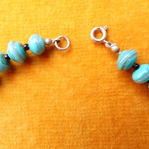 May include: A turquoise and silver necklace with a silver clasp. The beads are round and have a swirl pattern.