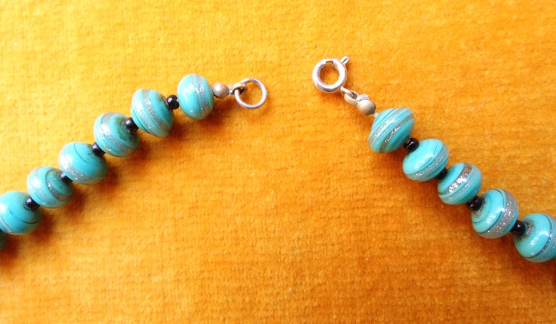 May include: A turquoise and silver necklace with a silver clasp. The beads are round and have a swirl pattern.