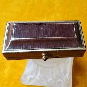May include: A small, rectangular, brown leather box with gold trim and a metal clasp. The box is closed.