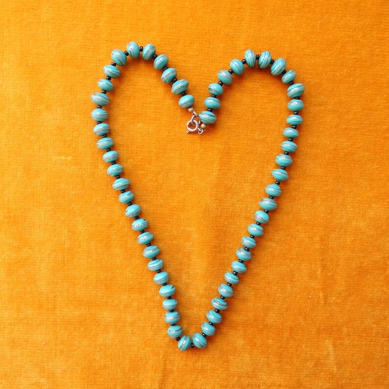 May include: A turquoise and silver necklace with round beads, shaped into a heart on a yellow background.
