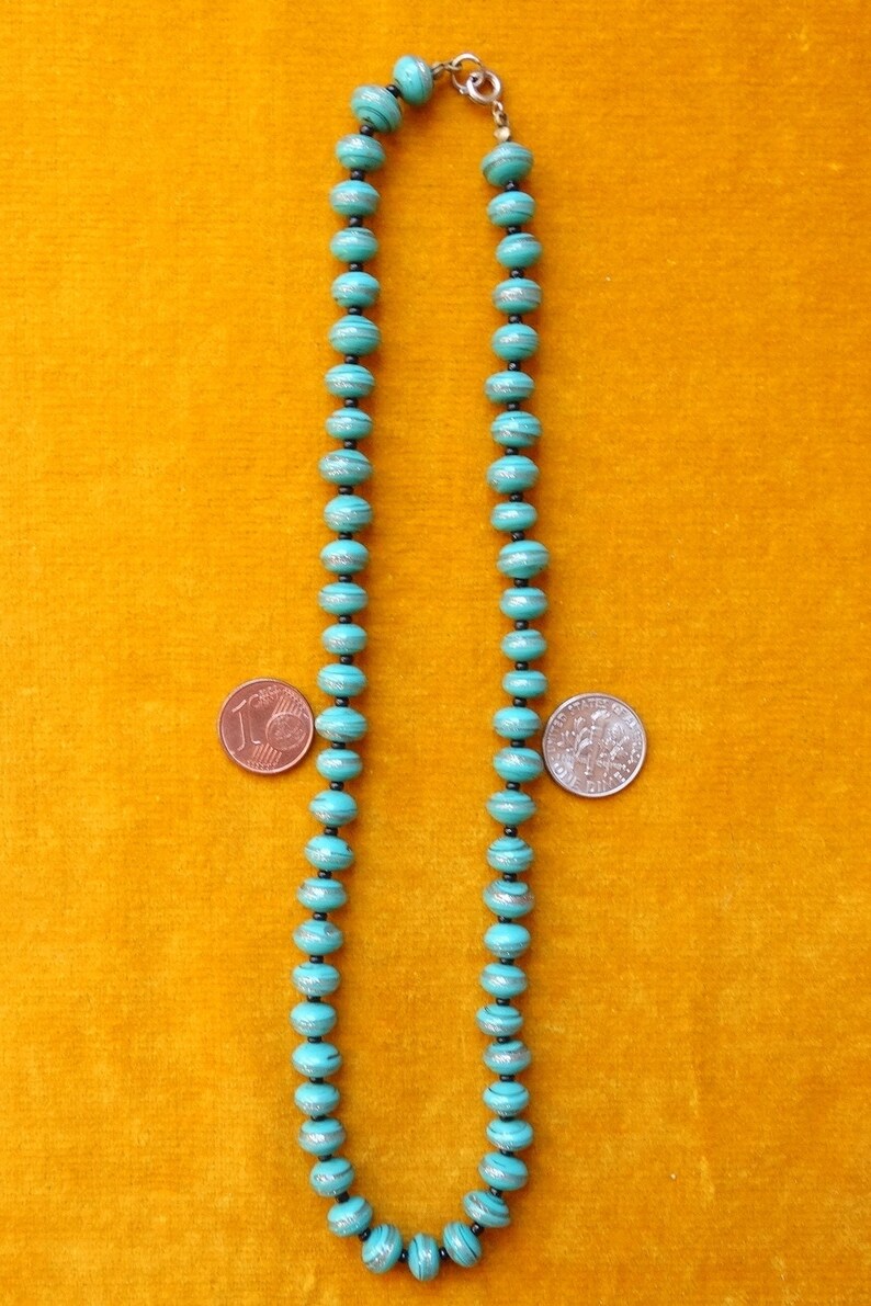 May include: A turquoise blue beaded necklace with silver accents. The beads are round and have a slightly textured surface. The necklace is approximately 46 cm long.