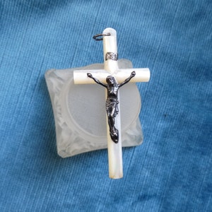 May include: A white mother of pearl crucifix with a silver-toned Jesus figure. The crucifix has a loop at the top for hanging.