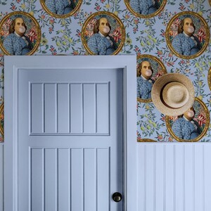 Puede incluir: Un pasillo azul con una puerta blanca y papel tapiz con un patrón repetido de retratos de Benjamin Franklin soplando una burbuja. El papel tapiz tiene un diseño floral con flores rosas, rojas y amarillas.