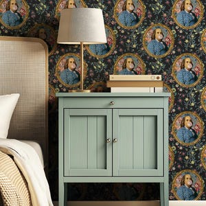 May include: A pale green bedside cabinet with two doors and a drawer, topped with a gold lamp and books. The wallpaper features portraits of Benjamin Franklin blowing bubble gum, framed in gold, against a dark floral background.
