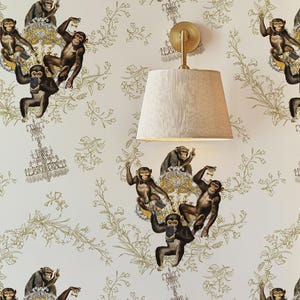 Puede incluir: Papel pintado con un patrón repetido de monos en varias poses, algunos sosteniendo teléfonos o bebidas, sobre un fondo crema con detalles florales dorados. También se ve un aplique de pared dorado con una pantalla beige.