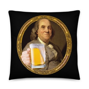 Puede incluir: Una almohada negra con un retrato enmarcado en oro de Benjamin Franklin sosteniendo un vaso de cerveza.