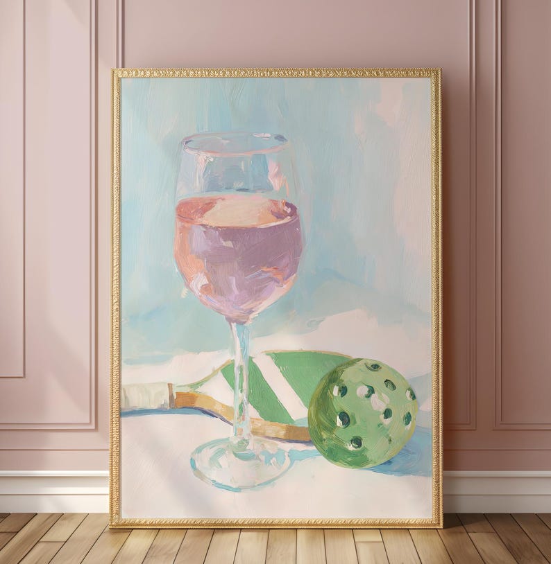 K&ouml;nnte beinhalten: Ein &Ouml;lgem&auml;lde zeigt ein Weinglas mit rosa Fl&uuml;ssigkeit, einen gr&uuml;nen Pickleball und einen Schl&auml;ger. Das Kunstwerk ist goldgerahmt und vor einem hellblauen und wei&szlig;en Hintergrund platziert. Der Stil ist impressionistisch.