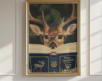 May include: A framed print featuring a deer wearing glasses and reading a book. The book has a blue cover with gold lettering and a deer illustration. The text on the book reads "Deer, Dreams Do Come True."