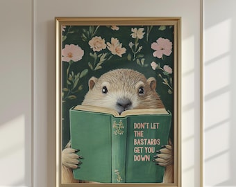 以下が含まれることがあります： 「DON'T LET THE BASTARDS GET YOU DOWN」のテキストが書かれた緑色の本を読んでいる、フレームに入ったアートプリント。背景は、ピンクの花が咲く濃い緑色の花柄です。プリントは金のフレームに入っています。