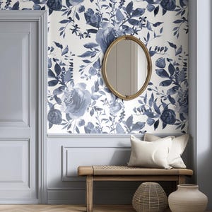 Puede incluir: Una habitación con papel pintado floral en tonos azules y blancos. Un espejo ovalado con marco dorado cuelga de la pared. Un banco de madera con cojines y jarrones decorativos se encuentra debajo del espejo, creando un diseño interior acogedor.