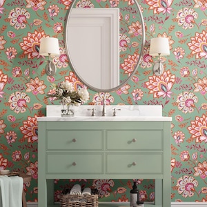 Puede incluir: Un mueble de baño verde salvia con cuatro cajones y un estante abierto, coronado por una encimera de mármol blanco. La pared presenta un papel pintado floral en tonos verdes, rosas y naranjas. Un espejo ovalado plateado y apliques.