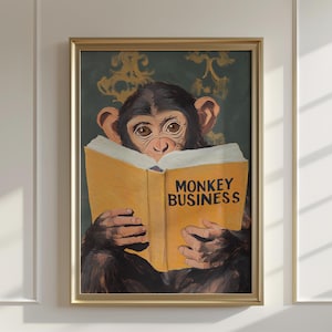 May include: A framed print showing a chimpanzee engrossed in a book titled "MONKEY BUSINESS". The chimp has brown fur and is set against a dark green backdrop with gold detailing. The frame is gold-coloured.