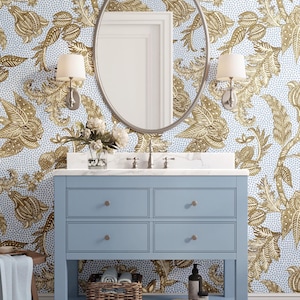 May include: A powder blue bathroom vanity with four drawers and a lower shelf, topped with a white countertop and a silver oval mirror. The wallpaper features a gold floral pattern on a light blue background. Two sconces flank the mirror.