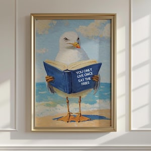 May include: A framed art print depicts a seagull standing on a beach, holding a blue book with the text "YOU ONLY LIVE ONCE EAT THE FRIES." The artwork has a gold frame and a background of a blue sky and clouds.