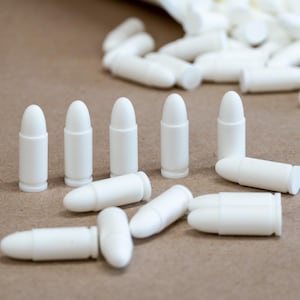 Puede incluir: Un grupo de balas de plástico blanco, algunas están tumbadas y otras están de pie sobre una superficie marrón.