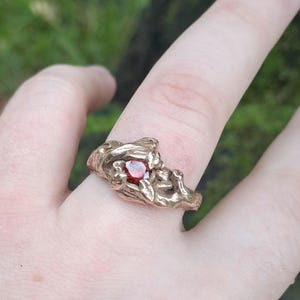 May include: A gold ring with a red gemstone set in a branch-like design.